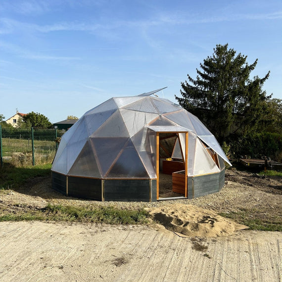 Serre dôme géodésique de 6,6 m en polycarbonate installée dans un jardin, sur un lit de gravier