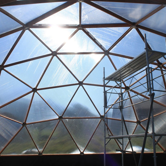 Intérieur d'une serre dôme de 10 m en cours de montage, triangles de polycarbonate et échafaudage