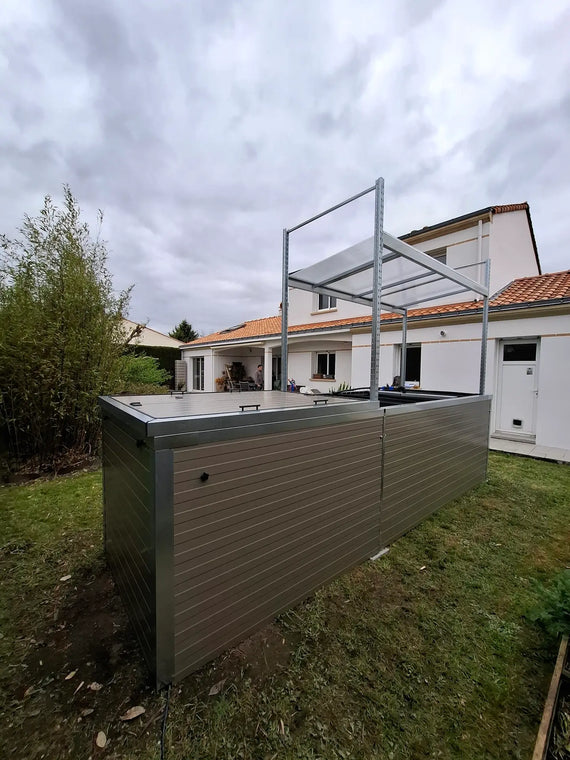 Symbiose vu de trois quarts au fond d'un jardin, habillage gris-brun et montants de la toiture