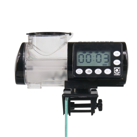 Distributeur automatique AutoFood noir fixé par sa pince sur le bord d'une vitre d'aquarium, écran allumé