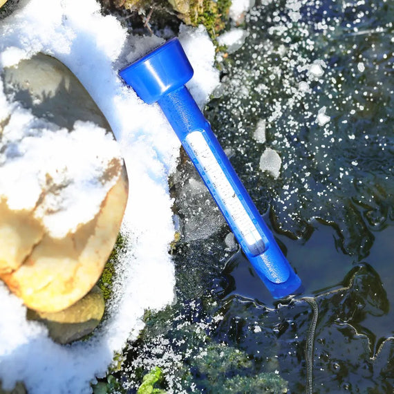 Termómetro flotante azul sobre el agua de un estanque en invierno, orilla cubierta de nieve