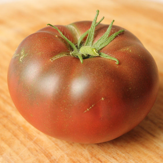 Tomate Noire de Crimée mûre en gros plan, peau brun pourpre et large collerette verte au pédoncule